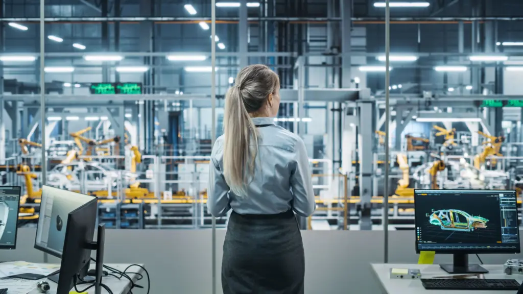 Ingenieurin steht in einer vernetzten Industrieanlage mit Roboterfertigungsstraße und überwacht die Produktion